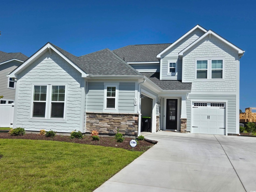 Craftsman-style home with driveway, a shingled roof, a front yard, an attached garage, and stone siding