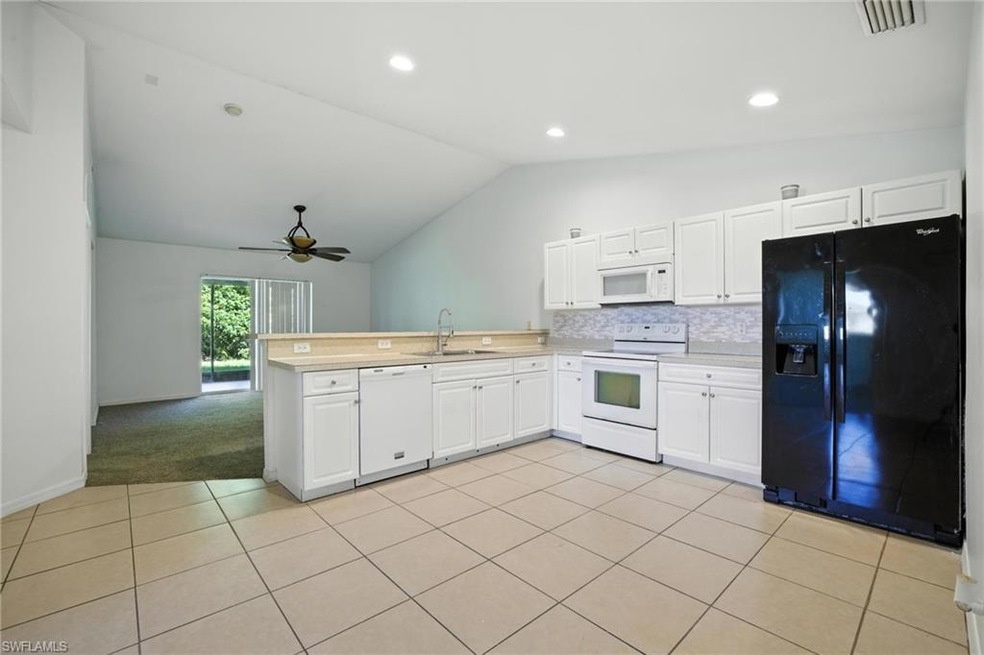 Kitchen featuring white appliances, vaulted ceiling, a peninsula, light countertops, and a ceiling fan