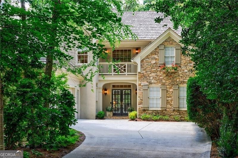 View of front of property featuring french doors, concrete driveway, stone siding, and a balcony