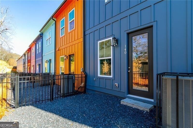 Doorway to property featuring fence, board and batten siding, and central AC