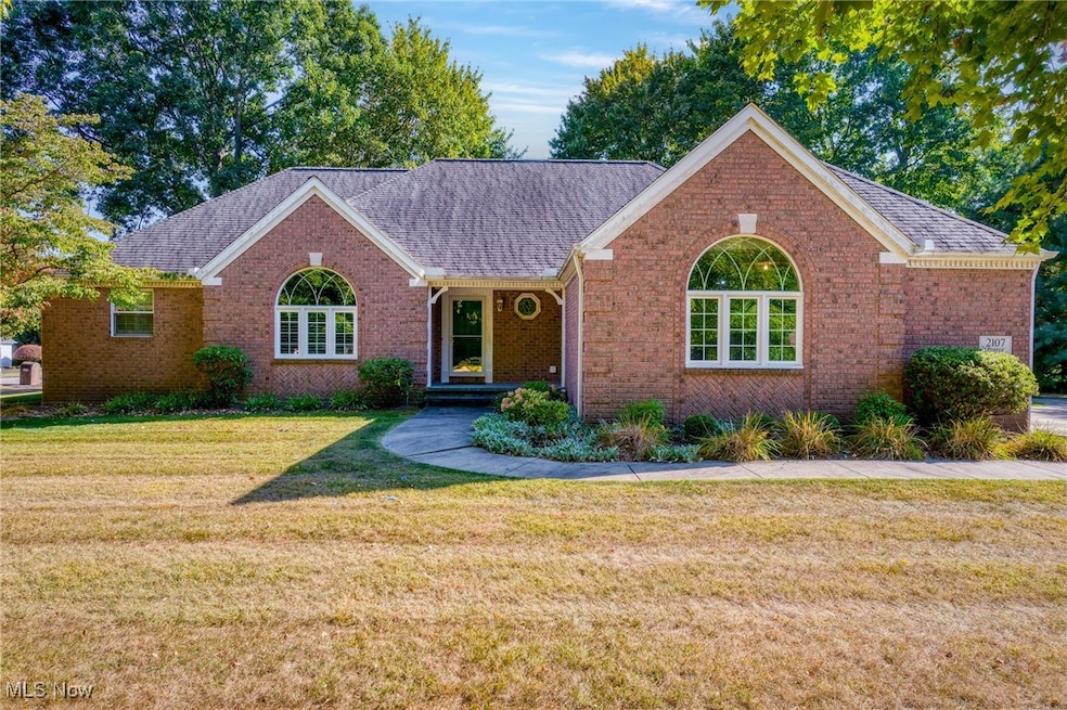 Ranch-style home featuring brick siding, a front lawn, roof with shingles, and covered porch