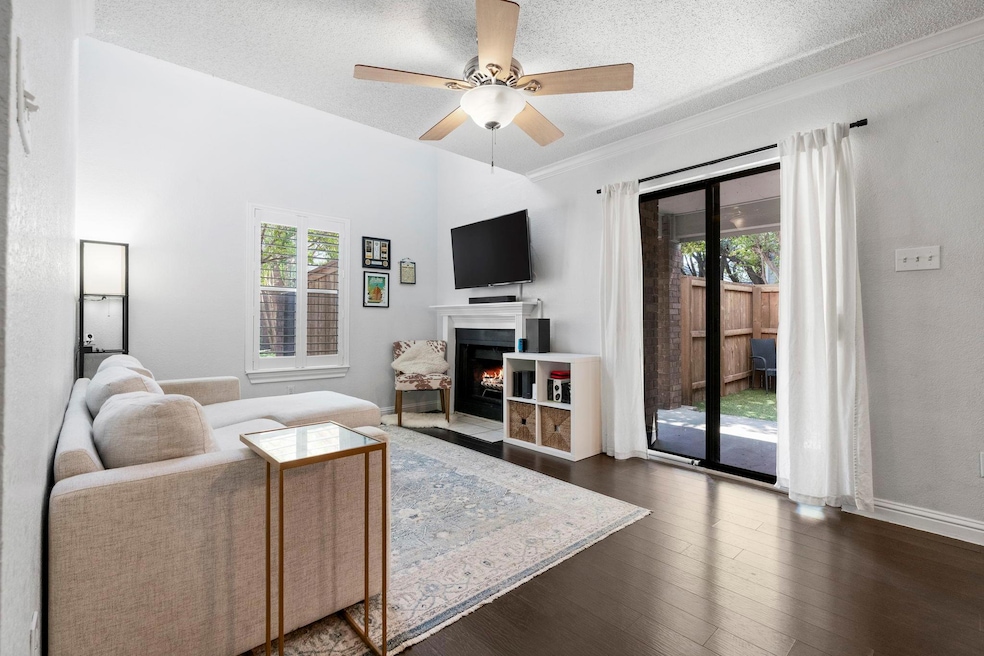 Living room featuring a textured ceiling, a fireplace with flush hearth, healthy amount of natural light, dark wood finished floors, and ceiling fan