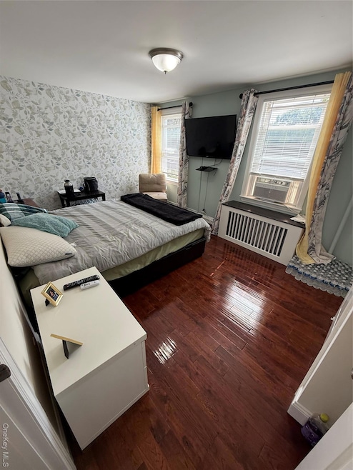 Bedroom featuring wallpapered walls, dark wood-type flooring, and cooling unit
