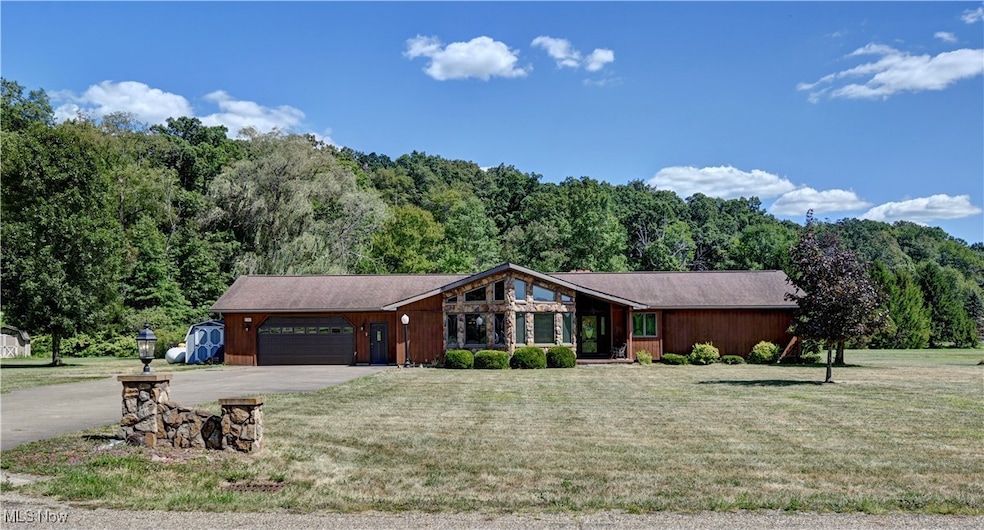 Mid-century inspired home with driveway, a front lawn, an attached garage, and a view of trees
