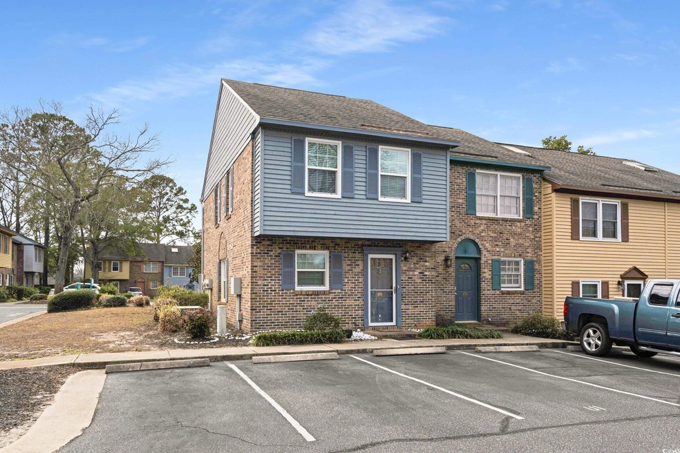 View of property with uncovered parking, brick sid