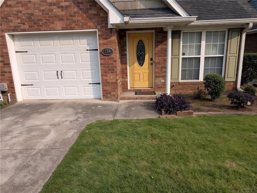 View of exterior entry with concrete driveway, brick siding, a garage, a lawn, and a shingled roof