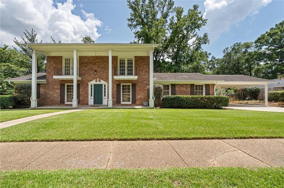 Neoclassical home with brick siding, a front lawn, an attached carport, and driveway
