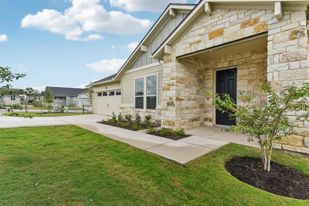 View of exterior entry featuring board and batten siding, stone siding, concrete driveway, and a lawn