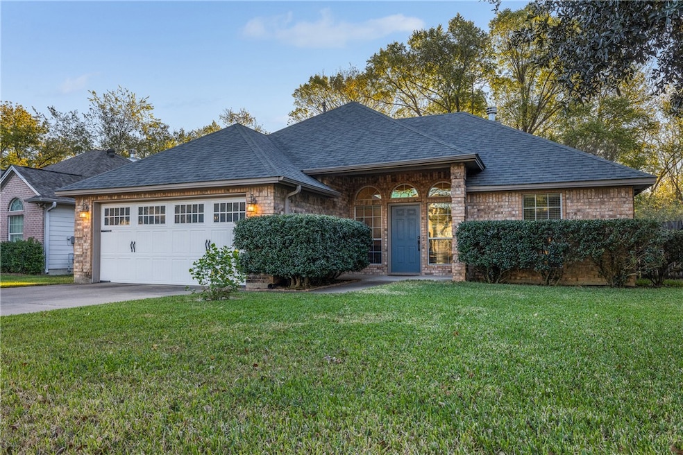 View of front elevation featuring roof with shingles, a front yard, driveway, and brick siding