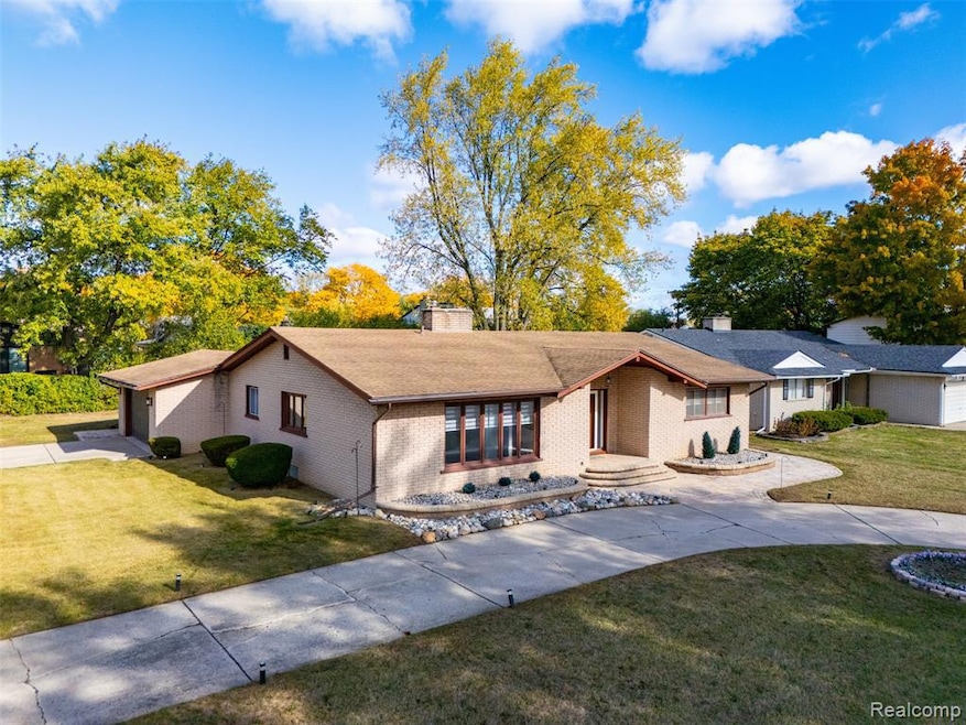 View of front facade featuring a front lawn, a chimney, brick siding, and driveway