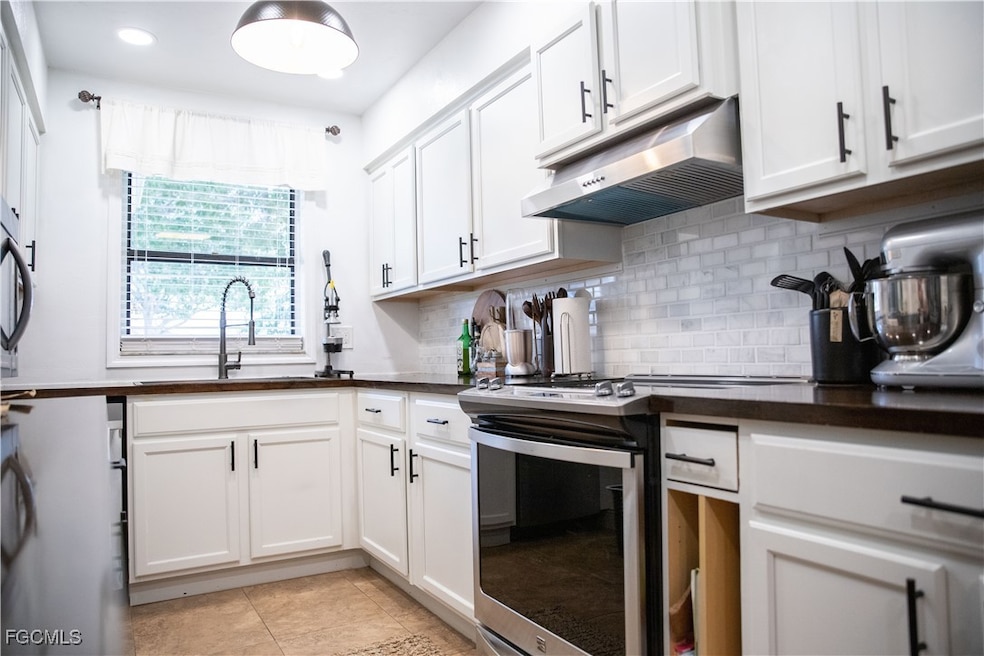 Kitchen with backsplash, stainless steel appliances, under cabinet range hood, white cabinetry, and light tile patterned floors