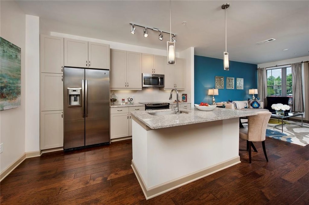 Kitchen featuring appliances with stainless steel finishes, sink, light stone counters, an island with sink, and dark hardwood / wood-style flooring