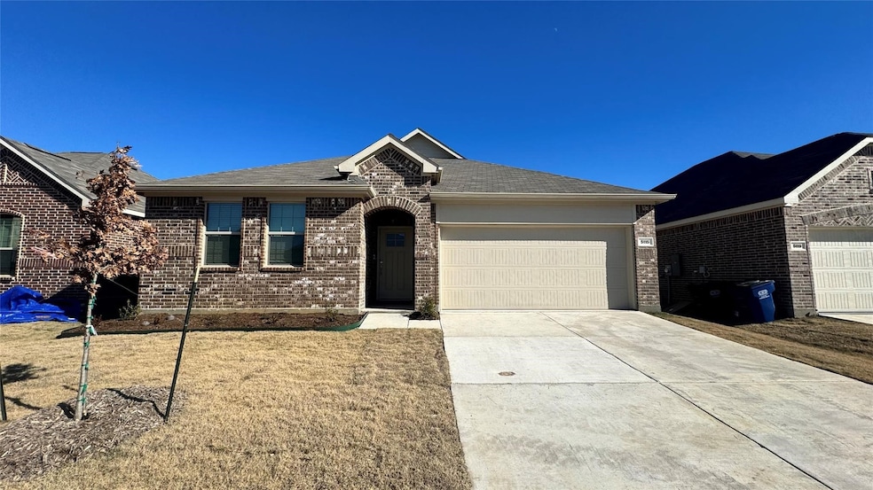 Single story home featuring concrete driveway, brick siding, an attached garage, and a front yard