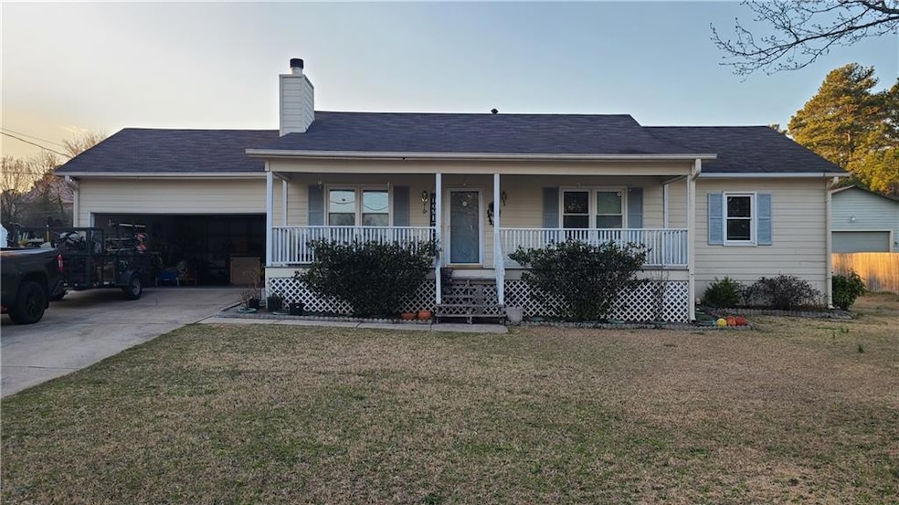 Single story home featuring a porch, a chimney, a front yard, driveway, and a garage