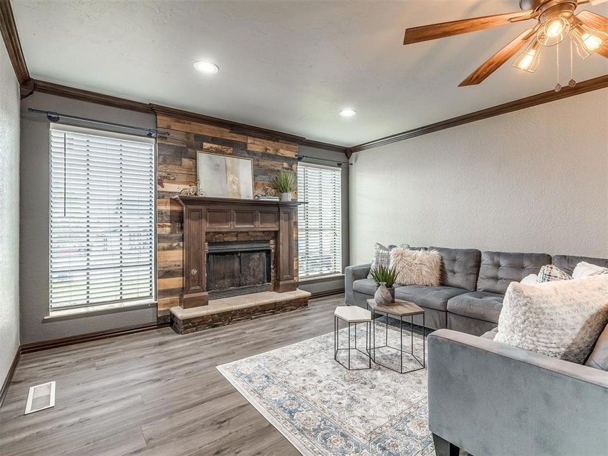 Living room with wooden walls, crown molding, a stone fireplace, ceiling fan, and light wood-type flooring