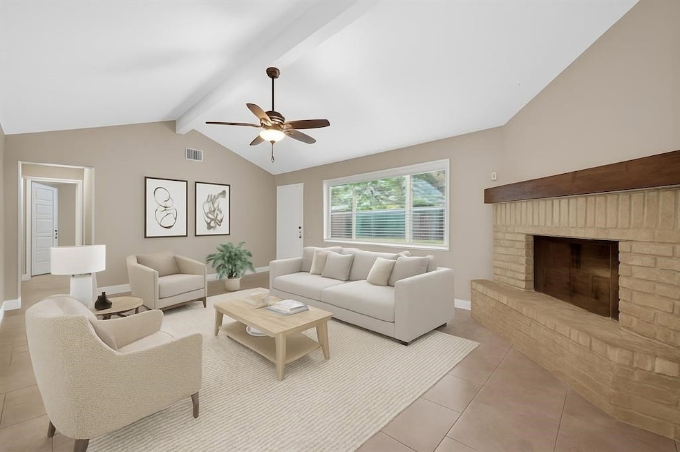 Spacious living room with neutral tones,
featuring a cozy brick fireplace, large
window for natural light, ceiling fan, and
tiled flooring. Ideal for relaxing or
entertaining.