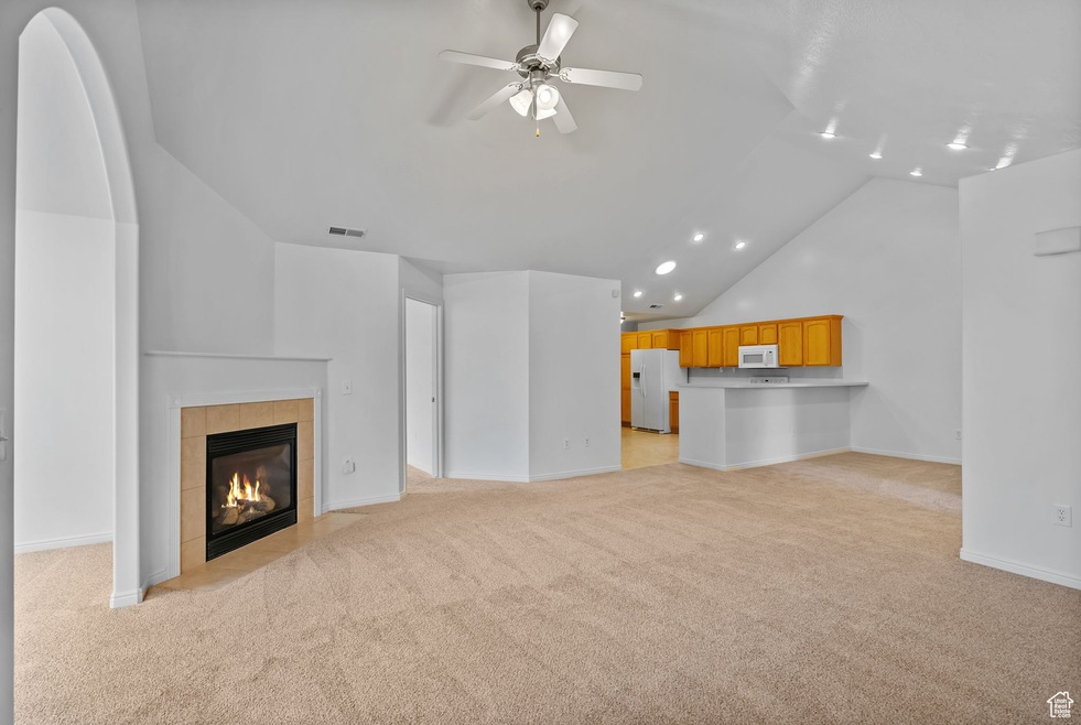 Unfurnished living room with light carpet, vaulted ceiling, a tiled fireplace, a ceiling fan, and recessed lighting