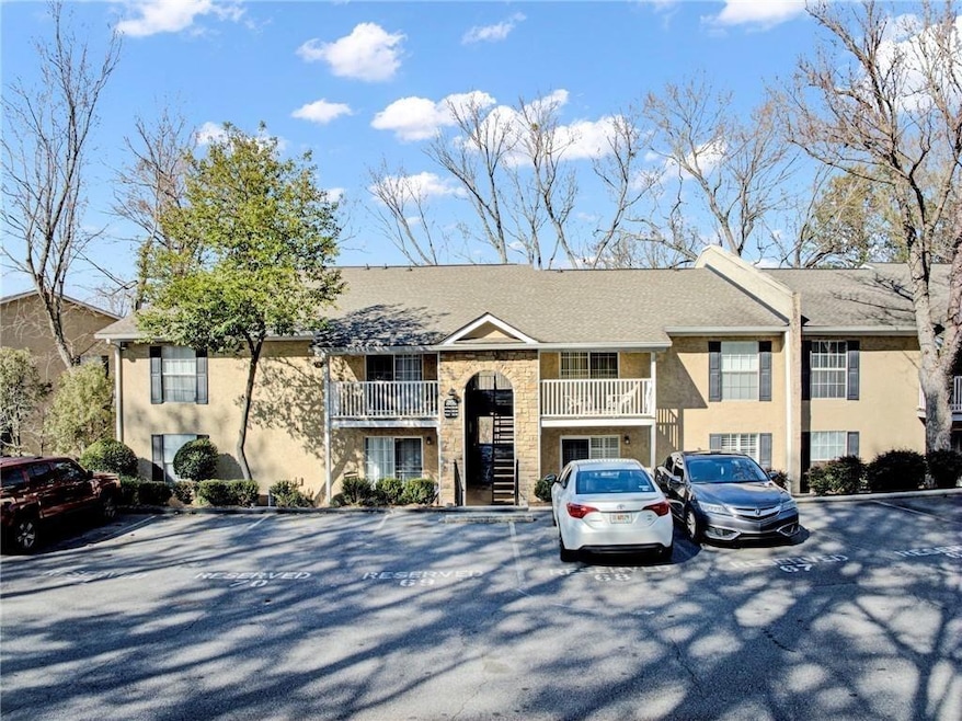 View of front of property featuring a balcony, uncovered parking, a shingled roof, and stone siding