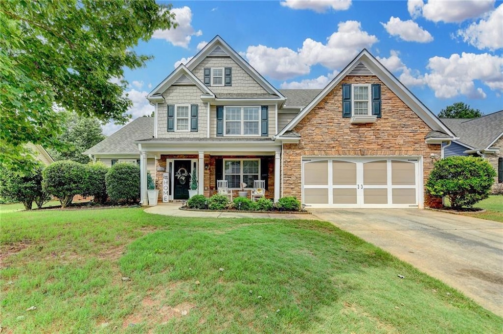 Craftsman-style home featuring driveway, covered porch, stone siding, a front yard, and a garage