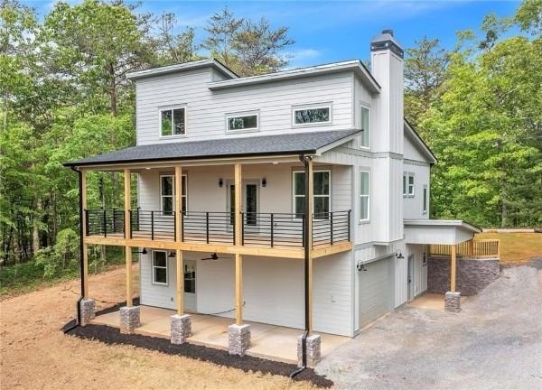 Rear view of property featuring a balcony, a chimney, an attached garage, asphalt driveway, and roof with shingles