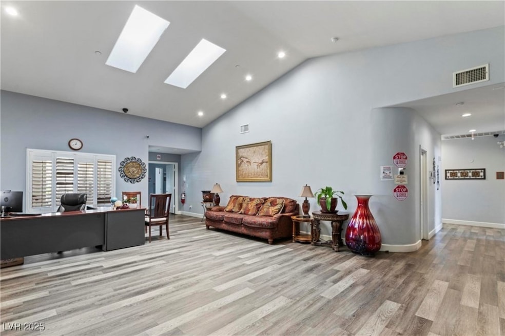 Living room with an office area, light wood finished floors, high vaulted ceiling, recessed lighting, and a skylight