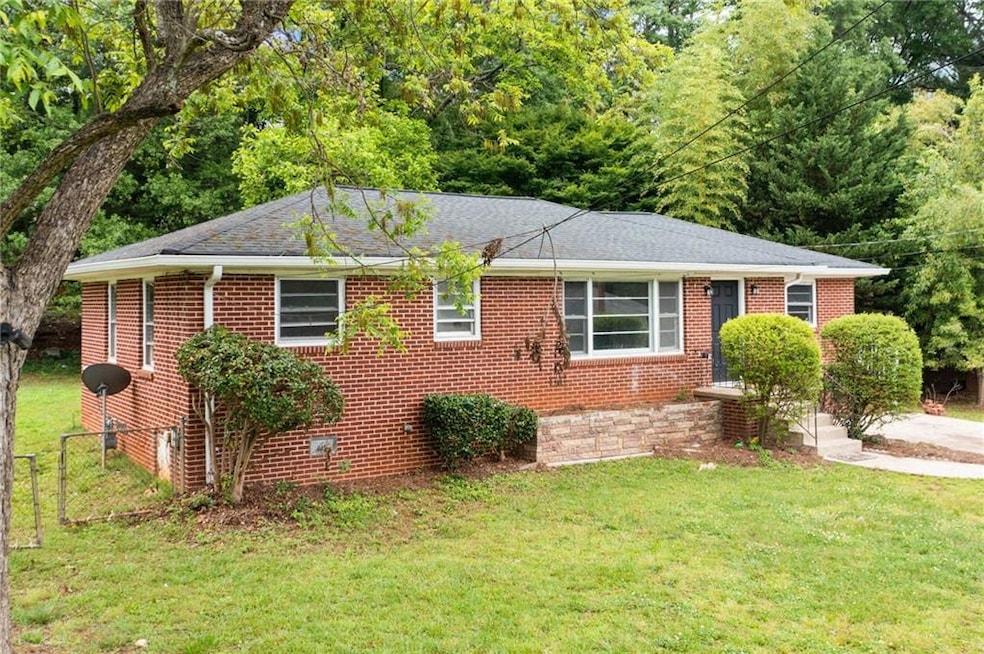 Ranch-style house with brick siding, roof with shingles, and a view of trees