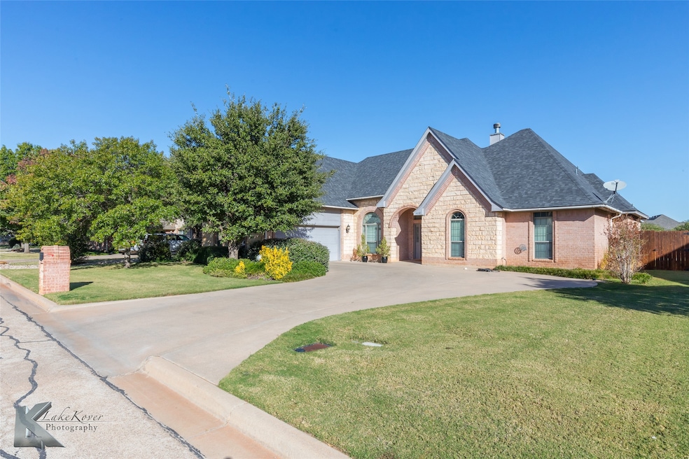 French country inspired facade with stone siding, driveway, a shingled roof, a chimney, and brick siding
