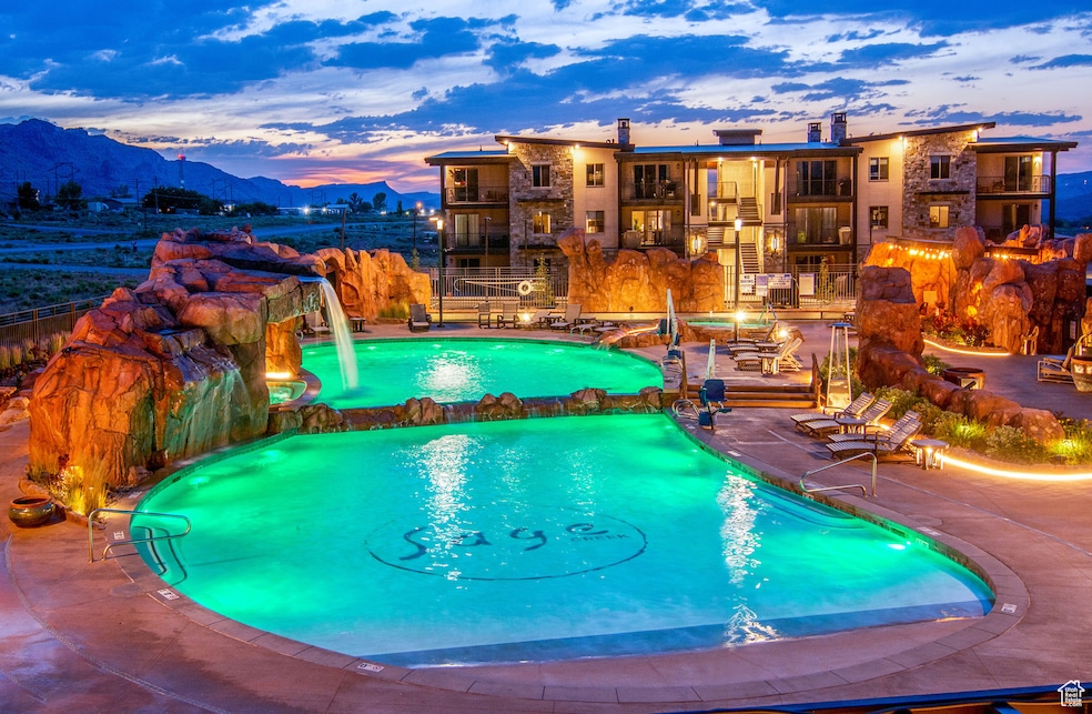 Pool at dusk featuring a patio, a mountain view, a pool with connected hot tub, and a balcony