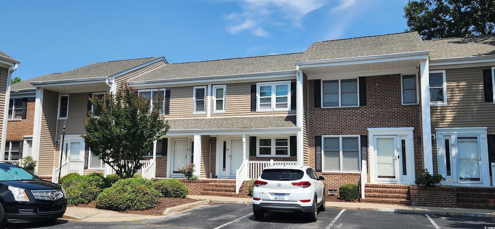Multi unit property with uncovered parking, a porch, a shingled roof, and brick siding