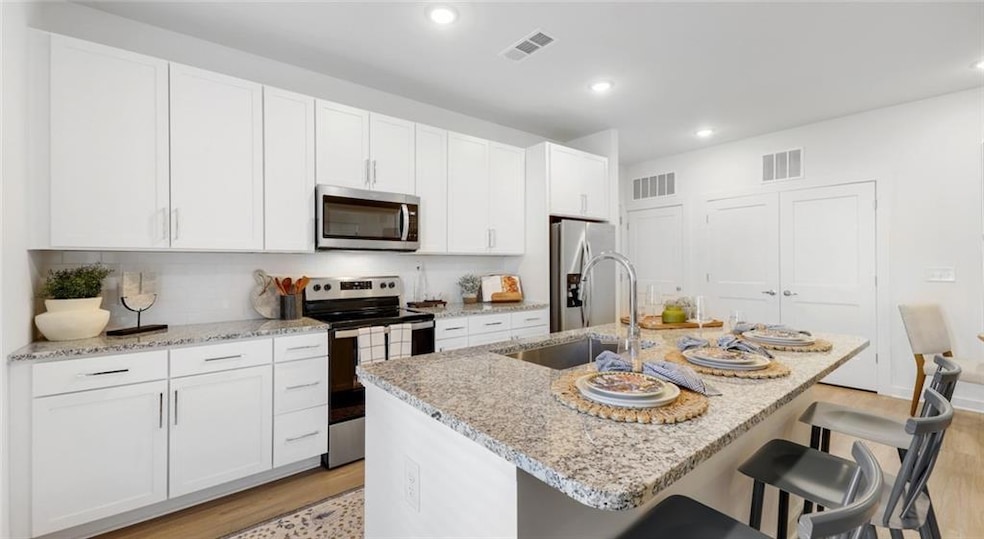 Kitchen with white cabinetry, light wood-type flooring, stainless steel appliances, an island with sink, and sink