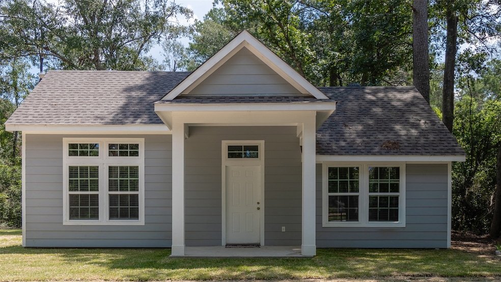Cozy single-story home with a blue exterior, white trim, and a gabled roof, featuring a covered entryway and multiple windows, nestled among trees.
