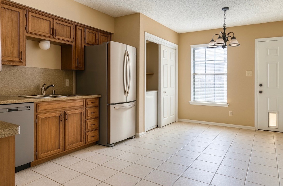 Kitchen with brown cabinetry, appliances with stainless steel finishes, decorative light fixtures, a chandelier, and a textured ceiling