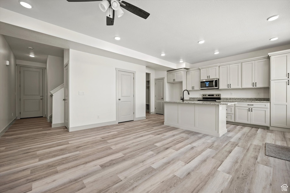 Kitchen featuring a kitchen island with sink, light wood-style flooring, a sink, appliances with stainless steel finishes, and light stone countertops