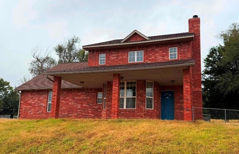 View of front of home featuring brick siding, a porch, a chimney, and a shingled roof