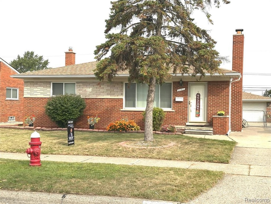 View of front facade with a chimney, a front yard, brick siding, roof with shingles, and a garage