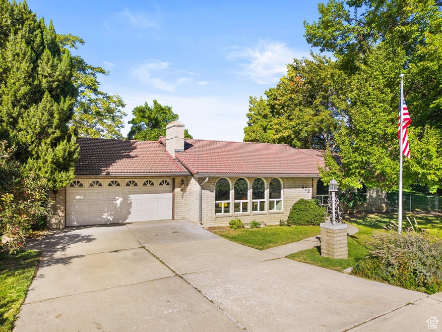View of front facade featuring a tiled roof, concrete driveway, a front yard, an attached garage, and a chimney
