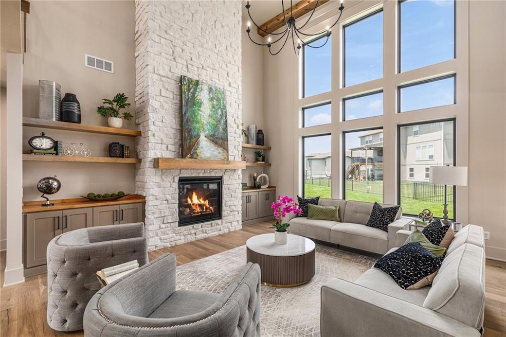 Living area featuring light wood finished floors, a towering ceiling, a stone fireplace, and a chandelier