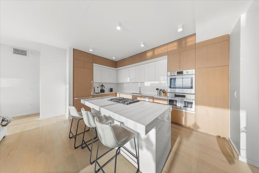 Kitchen featuring modern cabinets, light countertops, a kitchen breakfast bar, light wood-style flooring, and stainless steel appliances