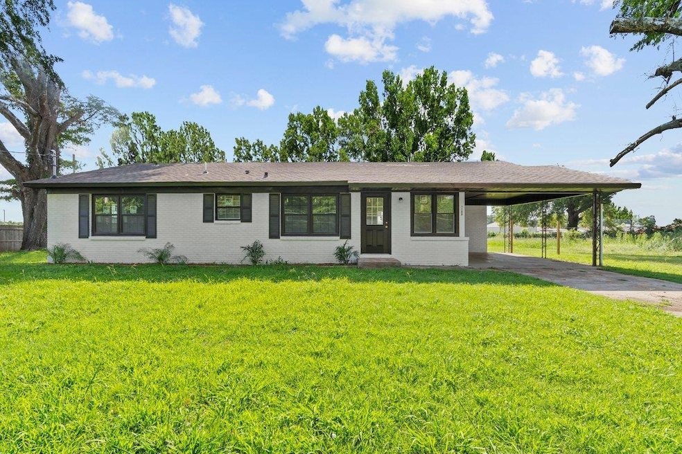 View of front facade featuring concrete driveway, an attached carport, a front lawn, and brick siding