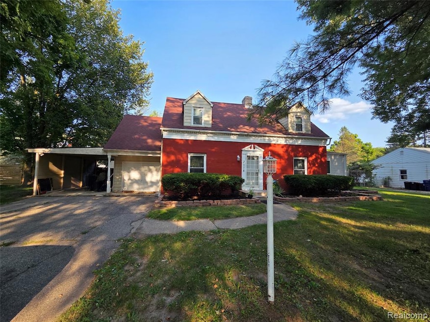 Cape cod home with an attached carport, a front yard, asphalt driveway, a chimney, and a garage