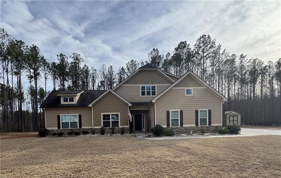 View of front of property featuring a shed, concrete driveway, a front yard, and stone siding