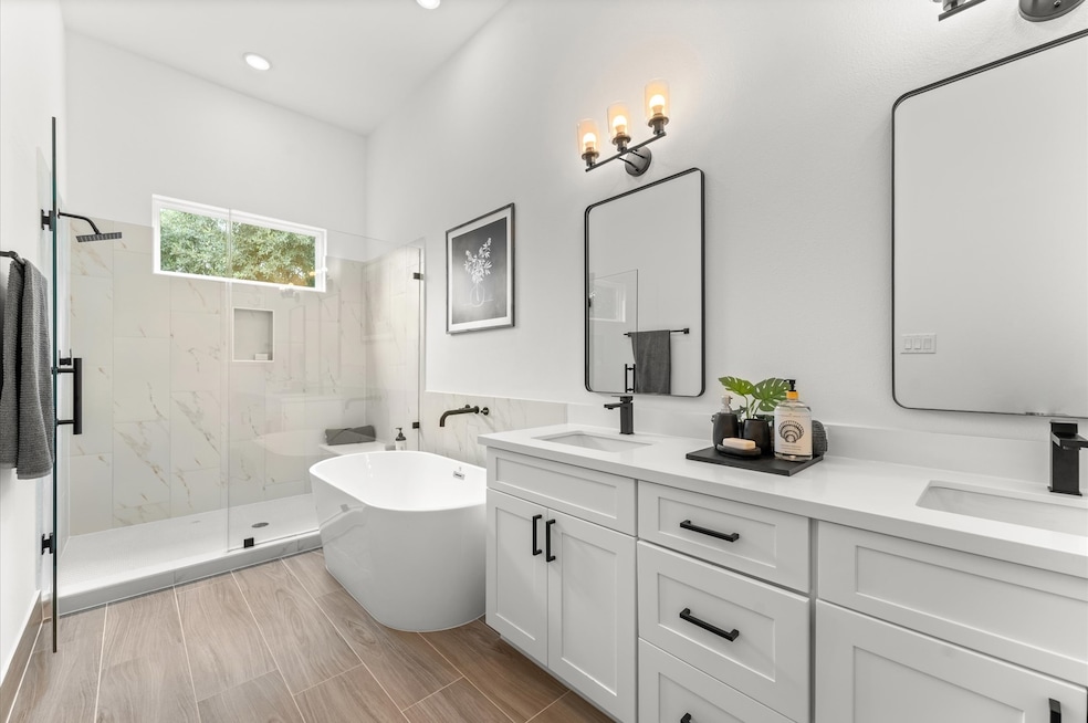 Elegant and serene primary bathroom designed to offer both style and functionality. The space features a luxurious soaking tub ideal for unwinding, a separate glass-enclosed shower for quick refreshes, and a sleek double vanity with ample countertop space and storage—perfect for busy mornings or relaxing evenings.