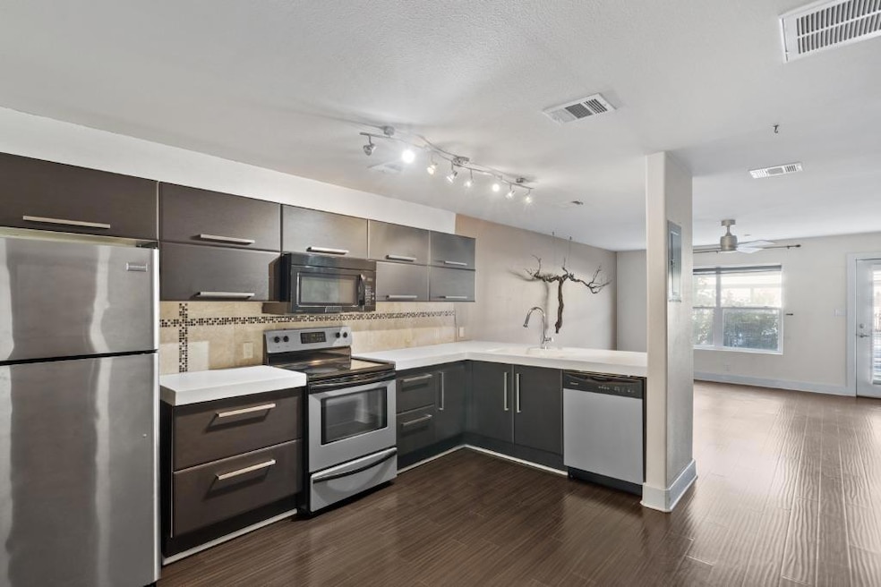Kitchen featuring stainless steel appliances, tasteful backsplash, ceiling fan, dark wood finished floors, and a peninsula