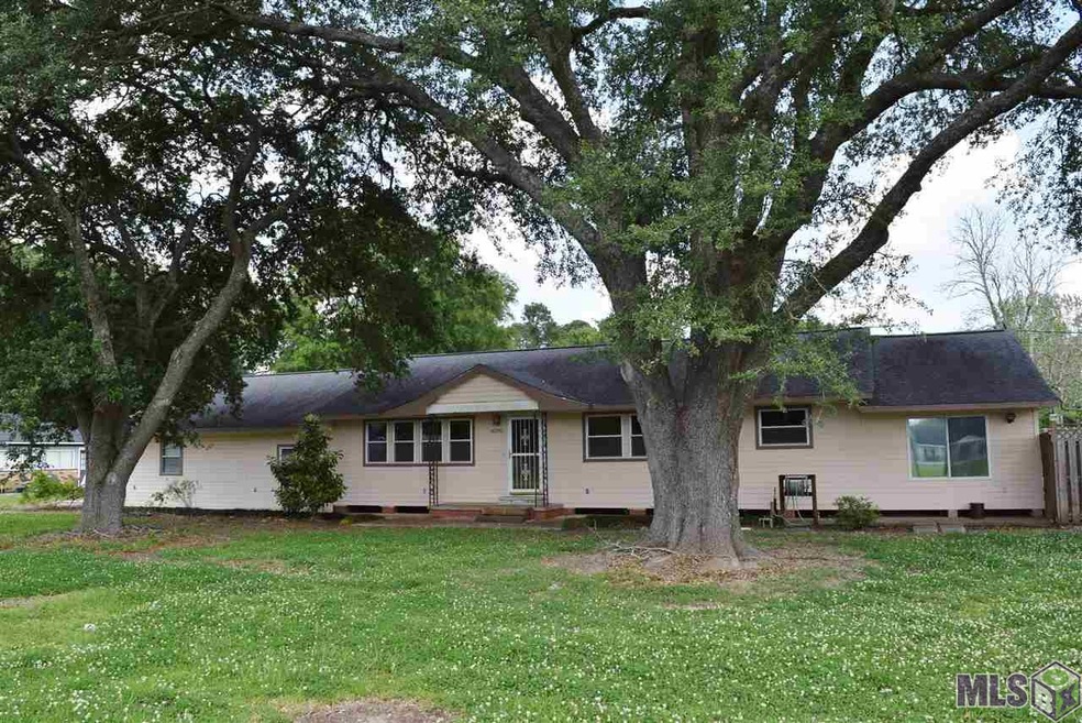 Two large Live Oak trees frame the house in the fr