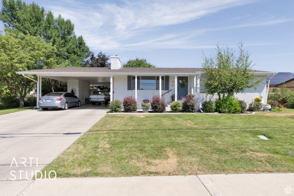 Ranch-style home with brick siding, concrete driveway, a chimney, an attached carport, and a front yard