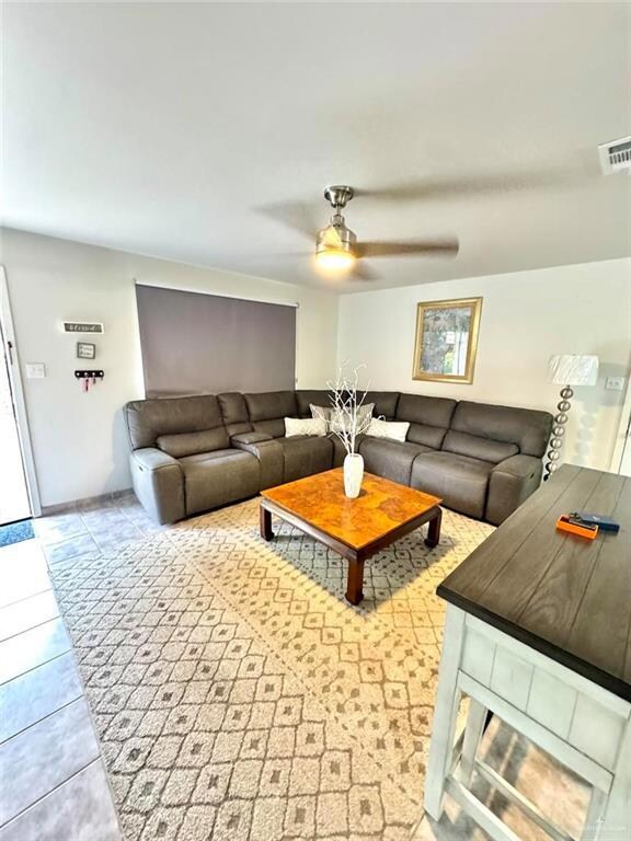 Living room featuring tile patterned floors, visible vents, and ceiling fan