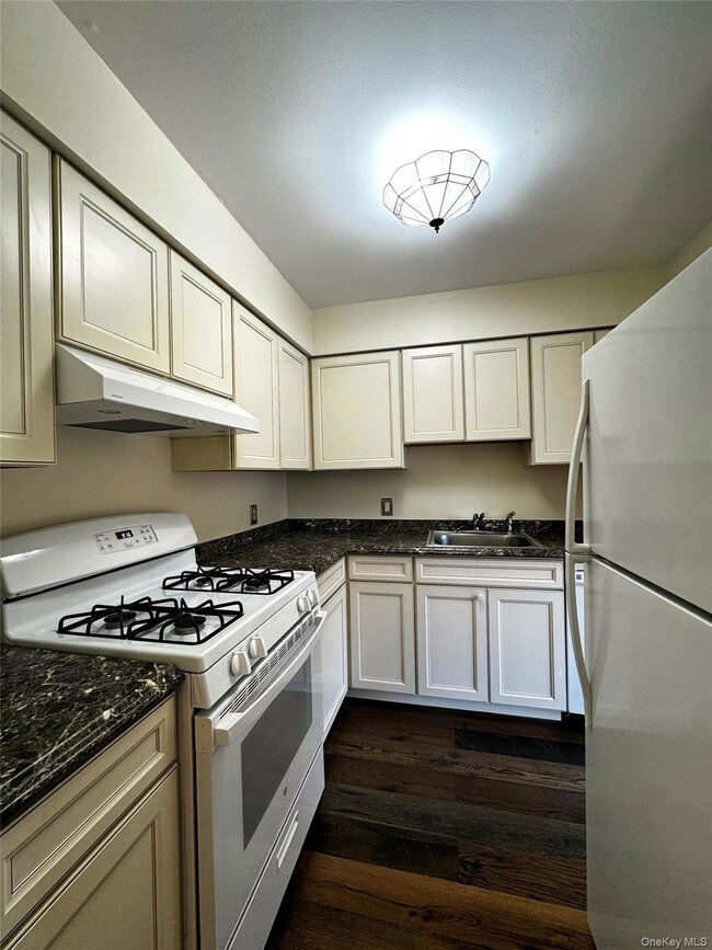 Kitchen with white appliances, under cabinet range hood, dark wood-style floors, and dark counters