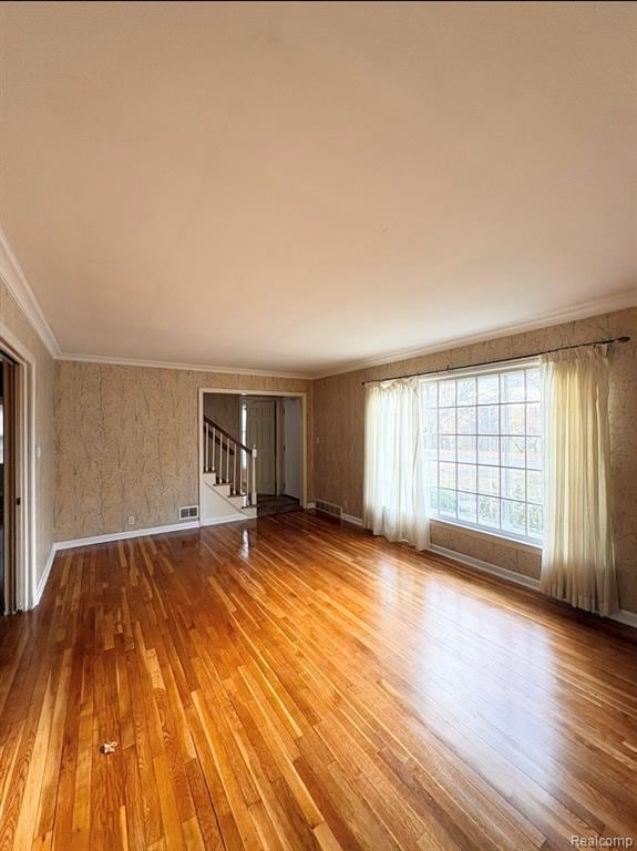 Empty room featuring crown molding, wallpapered walls, light wood-style flooring, and stairs