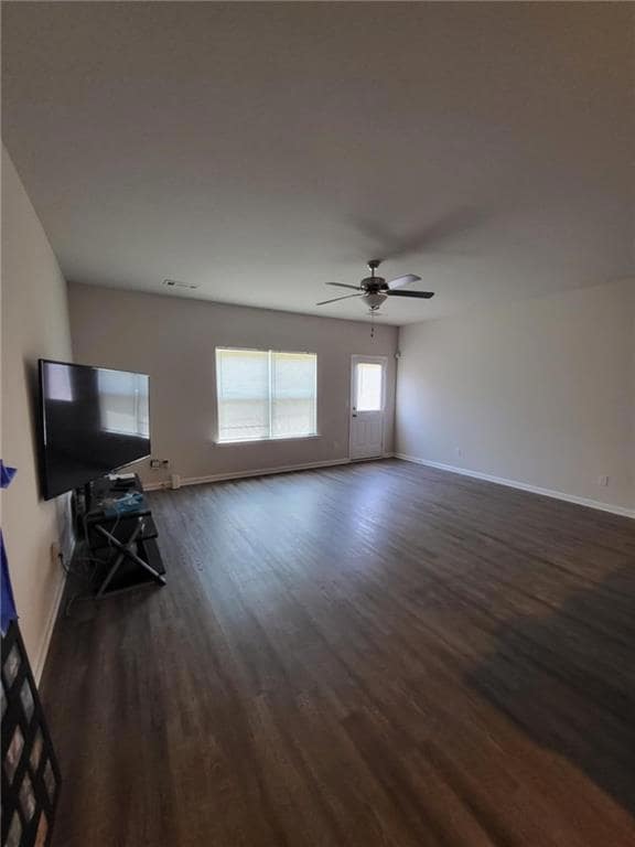 Unfurnished living room with dark wood-style floors, baseboards, and a ceiling fan