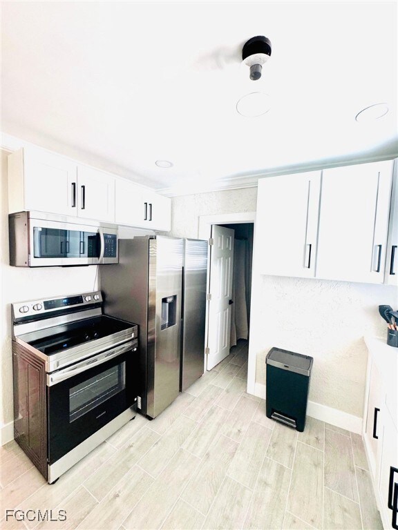 Kitchen featuring stainless steel appliances, white cabinetry, wood finish floors, and crown molding